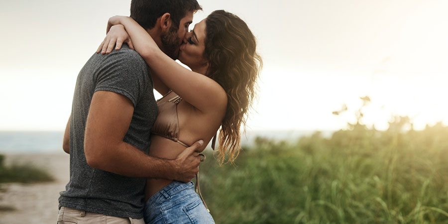 Attractive young couple who are dating kissing whilst in a passionate embrace at a beach location