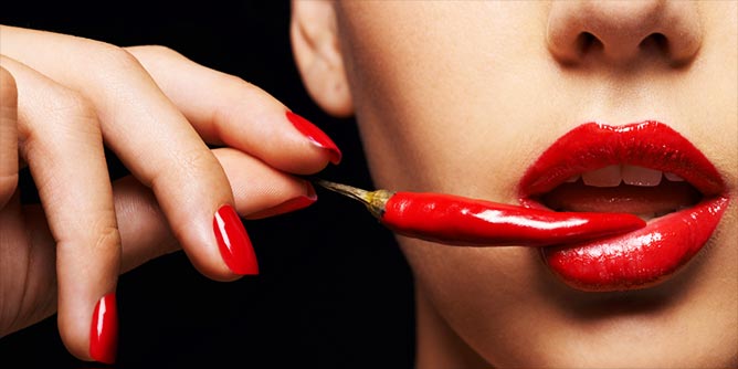 Woman holding a Thai red chilli to her open mouth