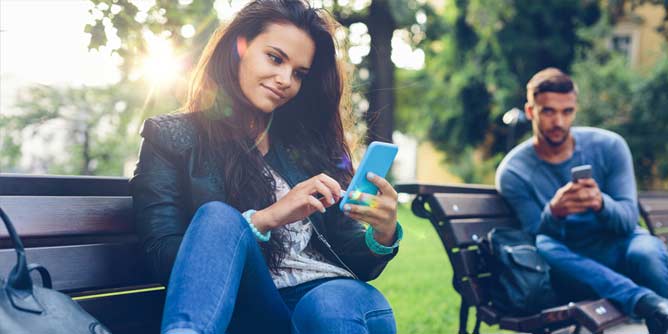 Young couple texting each other as they sit on separate park benches