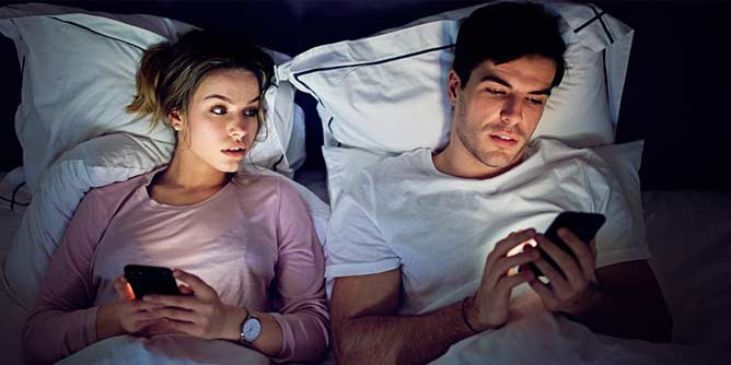 Couple in bed and woman is trying to see the message the man is reading on his mobile device