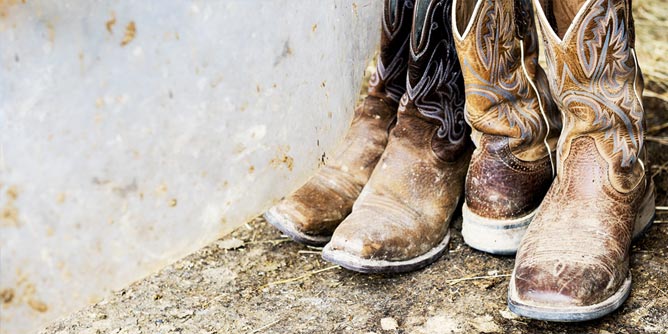 Two pairs of cowboy boots sitting outside in the dirt