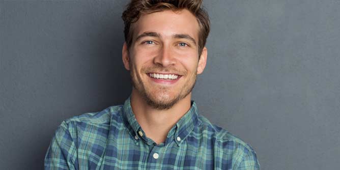 Handsome young man wearing a plaid shirt and smiling at the camera