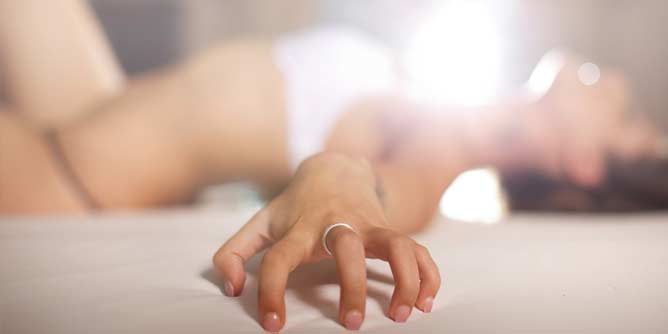 Close up of a woman's hand clutching the sheet as she orgasms