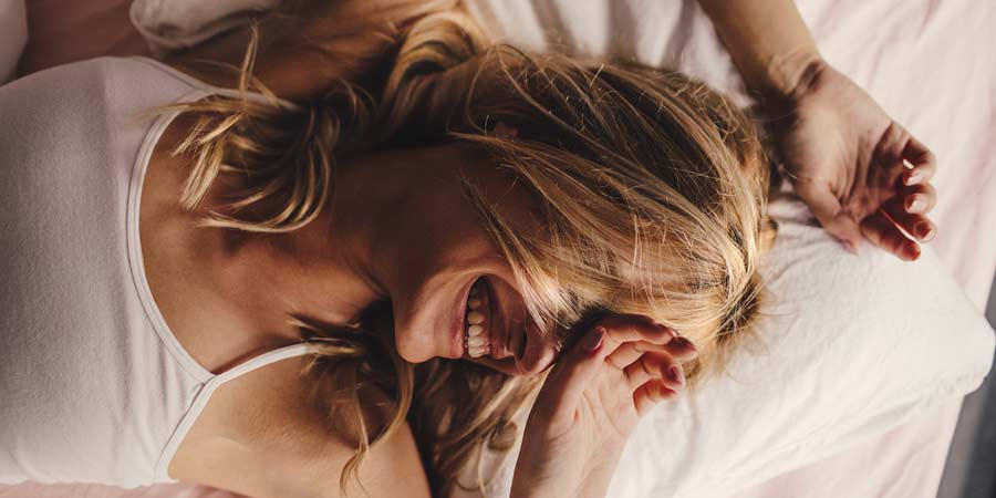 Woman lying in bed and smiling because she has experience a sleep orgasm