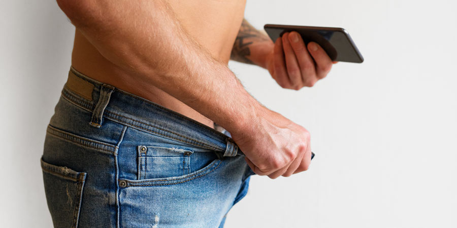 Bare chested man with his jeans unzipped about to take a photo with his mobile