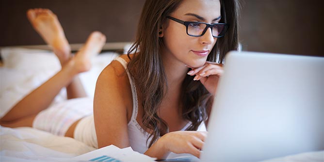 Attractive young woman wearing glasses using her laptop to create her dating profile