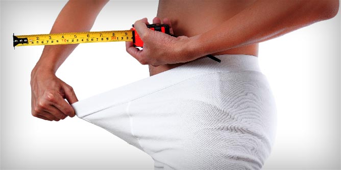 Man looking down his underpants while holding a measuring tape