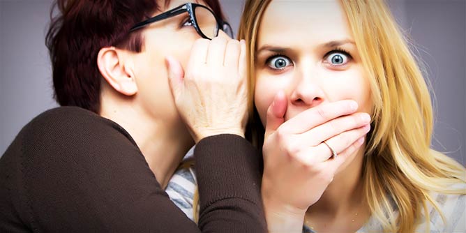 Woman whispering a secret to another woman who looks shocked
