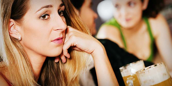 Woman with blonde hair sitting at a bar looking sad