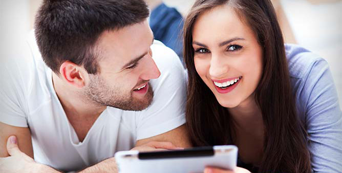 Young attractive couple smiling as they use their tablet to access a swingers site