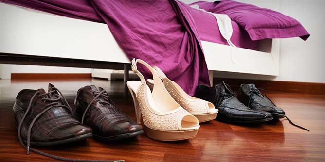 Three pairs of shoes sitting beside a bed while their owners have a threesome
