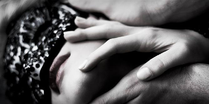 Close up of a woman wearing a carnival mask as a man caresses her face 