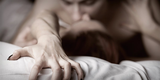 Woman's hand grips the bedsheet in a moment of passion